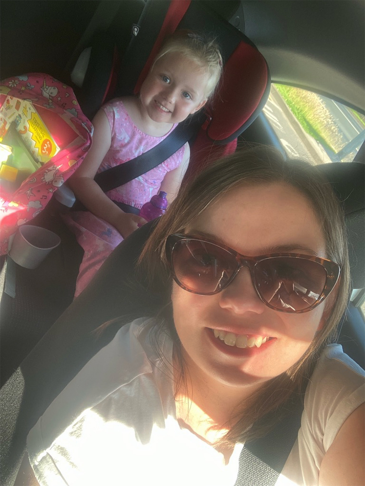 In car selfie with Liz in the foreground and daughter sat in a car seat on the back seat, both smiling